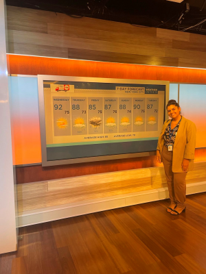 Bri Vig standing next to a weather forecast